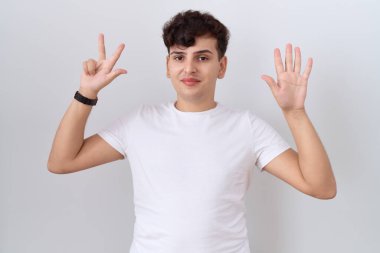 Gündelik beyaz tişört giyen genç adam 8 numarayı gösterip işaret ederken kendinden emin ve mutlu gülümsüyor.. 