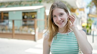 Kahvecinin terasında kendinden emin gülümseyen genç sarışın kadın.