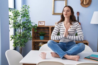 Young woman doing yoga exercise sitting on table at home