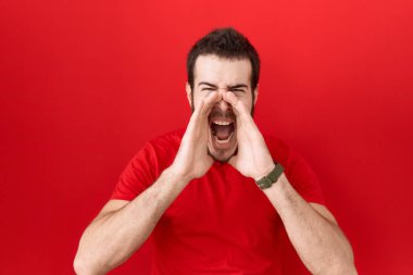 Gündelik kırmızı tişört giyen genç İspanyol adam elleri ağzında kızgın bir şekilde bağırıyor. 
