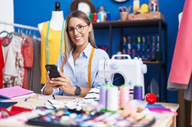 Elbise fabrikasında akıllı telefon kullanan, kendine güvenen, güzel İspanyol bir terzi.