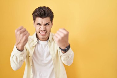 Sarı arka planda öfkeli ve kızgın duran genç İspanyol adam öfkeyle bağırırken kızgın ve öfkeli yumruklar sallıyor. öfke ve agresif konsept. 