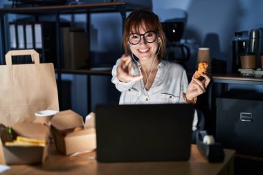 Genç ve güzel bir kadın bilgisayar bilgisayarı kullanıyor ve yemek yiyor. Gülümsüyor, avuç içi kadar yardım ve kabul görüyor.. 