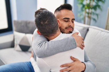 Two men couple hugging each other sitting on sofa at home