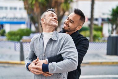Two men couple smiling confident hugging each other at street