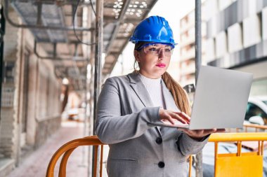 Young beautiful hispanic woman architect using laptop at street