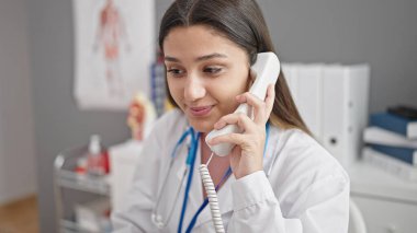 Genç, güzel İspanyol kadın doktor gülümseyerek klinikte telefonla konuşuyor.
