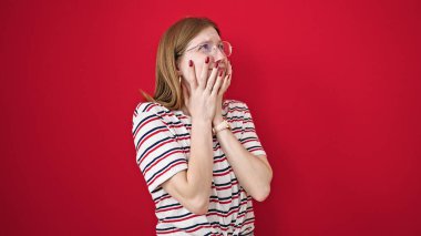 Genç sarışın kadın, izole edilmiş kırmızı arka planda dehşet verici hareketler yapıyor.