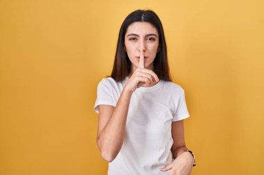 Sarı arka planda duran genç ve güzel bir kadın sessiz olmak istiyor. sessizlik ve gizli konsept. 