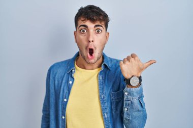 Mavi arka planda dikilen İspanyol genç adam elleri yana doğru işaret ederek şaşırdı, ağzı açık hayret içinde kaldı.. 