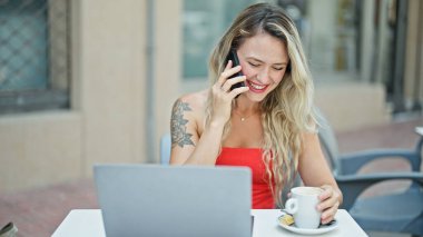 Genç sarışın kadın, kafenin terasında bilgisayarla konuşuyor.