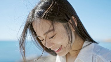 Genç Çinli kadın kendinden emin bir şekilde gülümsüyor ve deniz kenarına bakıyor.