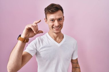 Pembe arka planda duran beyaz bir adam gülümsüyor ve el hareketleriyle küçük boy işareti yapıyor ve kameraya bakıyor. ölçüm kavramı. 