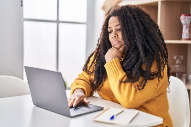 Evde masada dizüstü bilgisayar kullanan Afrikalı Amerikalı bir kadın.