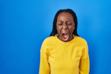 Güzel siyah bir kadın mavi arka planda öfkeli ve kızgın bir şekilde bağırıyor öfkeyle bağırıyor. öfke ve agresif konsept. 