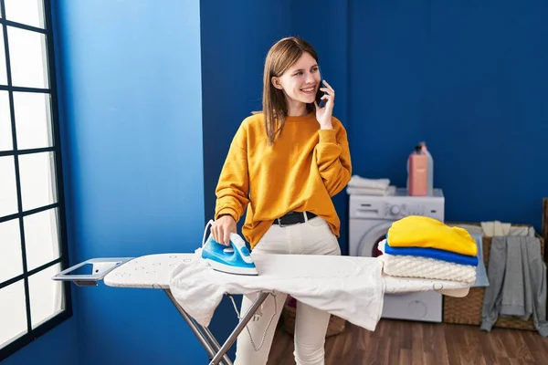 Genç Sarışın Kadın Akıllı Telefonda Konuşuyor Çamaşırhanede Giysileri Ütülüyor — Stok fotoğraf