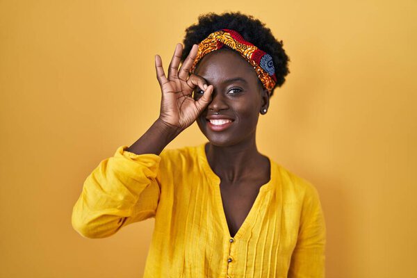 African young woman wearing african turban doing ok gesture with hand smiling, eye looking through fingers with happy face.
