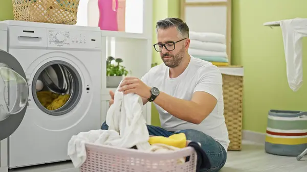 Grey-haired man washing clothes at laundry room