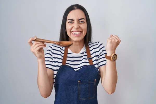 Young Brunette Woman Wearing Apron Tasting Food Holding Wooden Spoon — Stock Photo, Image