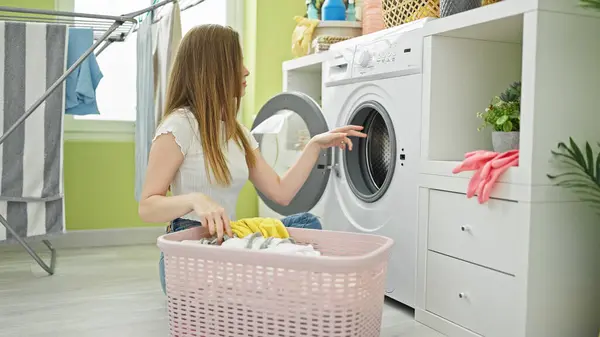 Young blonde woman washing clothes at laundry room