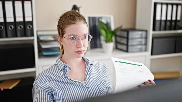 Young blonde woman business worker using documents as a hand fan at office