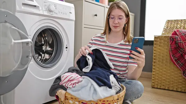 年轻的金发女人在洗衣房用智能手机洗衣服 — 图库照片
