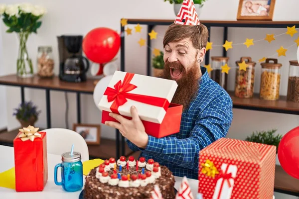 Young redhead man celebrating birthday unpacking gift at home