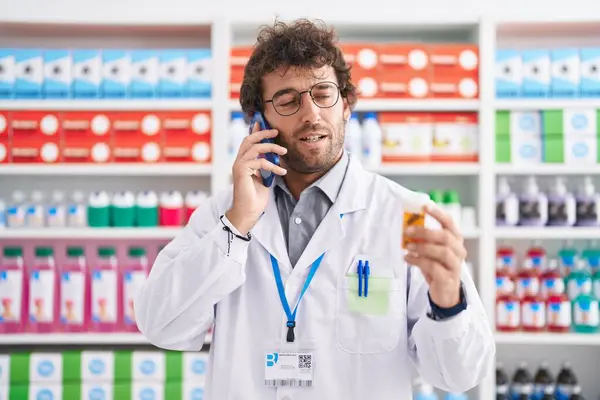 Joven Farmacéutico Hispano Sosteniendo Botella Pastillas Hablando Teléfono Inteligente Farmacia — Foto de Stock