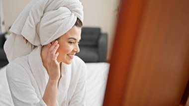 Bornoz giymiş genç ve güzel bir İspanyol kadın yatak odasındaki aynaya bakıyor.