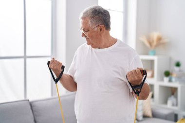 Evde elastik bant eğitimi alan orta yaşlı, kır saçlı bir adam.