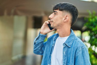 Young hispanic man talking on smartphone with serious expression at street