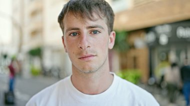 Sokakta ciddi bir ifadeyle duran beyaz bir genç.