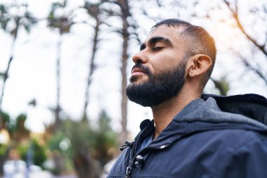Young hispanic man breathing with closed eyes at park