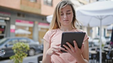 Kahve dükkanının terasında dokunmatik ped kullanan genç sarışın kadın.