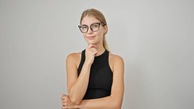 İzole edilmiş beyaz arka planda şüpheli bir ifadeyle duran genç sarışın kadın.