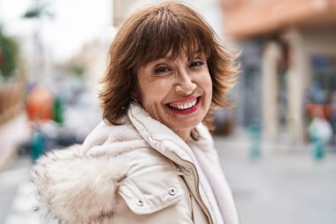 Orta yaşlı bir kadın sokakta kendine güvenerek gülümsüyor.