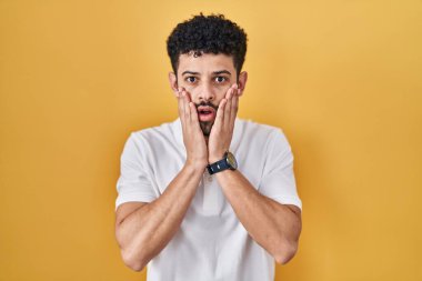 Sarı arka plan üzerinde duran Arap adam korkmuş ve şok olmuş, şaşırmış ve şaşırmış bir yüz ifadesi var. 