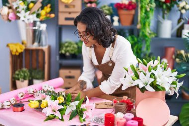 Young beautiful hispanic woman florist make bouquet of flowers at flower shop