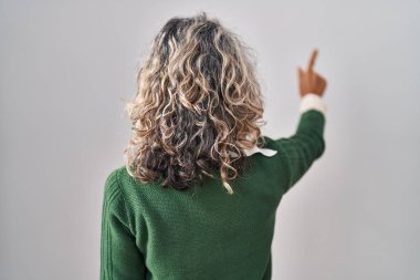 Orta yaşlı bir kadın beyaz arka planda dikiliyor. Geriye doğru poz veriyor. 