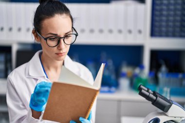 Young caucasian woman scientist reading book at laboratory