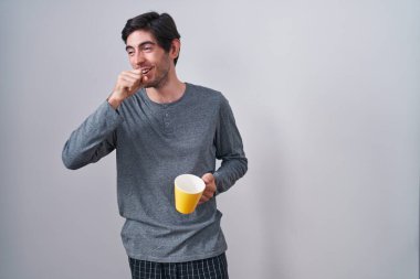 Genç İspanyol bir adam pijama giyip bir fincan kahve içiyor kendini iyi hissetmiyor ve soğuk algınlığı veya bronşitin belirtisi olarak öksürüyor. sağlık hizmeti kavramı. 