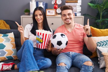 Genç İspanyol çift futbol holiganları top tutarken ve patlamış mısır yerken mutlu mesut el ve parmak kenarı işaret ediyorlar. 