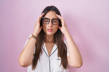 Genç esmer kadın, pembe arka planda duran gözlüklü, başı ağrıyan bir kadın, stres yüzünden. migren ağrısı. 
