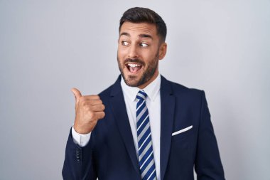 Yakışıklı İspanyol takım elbiseli ve kravatlı mutlu yüzlü gülümseyen ve baş parmağıyla yüzünü gösteren adam.. 