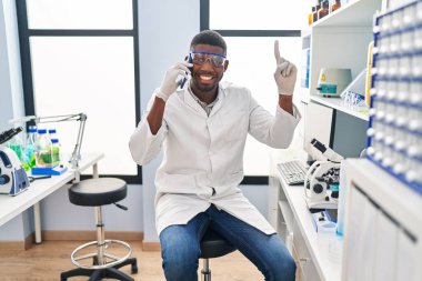 Bilim adamlarının laboratuvarında çalışan Afrikalı Amerikalı bir adam telefonda konuşurken bir fikir veya soruyla gülümsüyor ve mutlu bir yüzle işaret ediyor. 