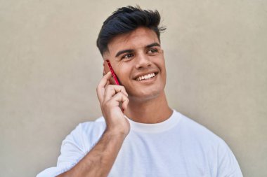 Genç, İspanyol asıllı, kendine güvenen, izole beyaz arka planda akıllı telefondan konuşan adam.