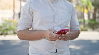 Young hispanic man using smartphone at park