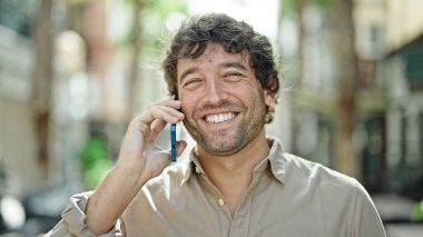 Genç İspanyol adam gülümsüyor. Kendine güveniyor. Sokakta akıllı telefondan konuşuyor.