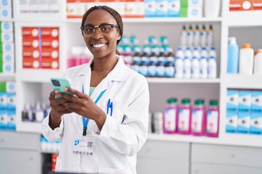 Eczanede çalışan akıllı telefonu kullanan Afrikalı Amerikalı kadın eczacı.