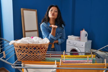 Genç Asyalı kadın çamaşır ipine kıyafet asıyor kameraya bakıyor ve havada bir öpücük savuruyor güzel ve seksi. aşk ifadesi. 